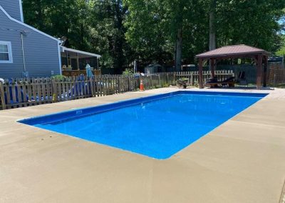 A finished pool renovation with the new pool, concrete with a beautiful yard behind it.